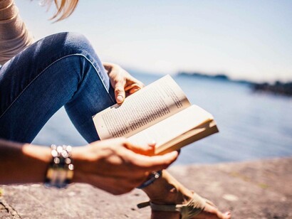 A woman by the sea reading a novel by Virginia Woolf on a day with clear skies