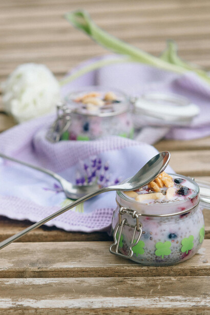 Two glass jars of chia seed pudding with berries and nuts served on a wooden table with lavender cloth