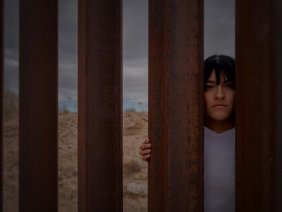 A young Mexican woman poses near the international border barrier wall between the USA and Mexico