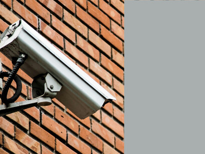 A security camera mounted on the side of a brick building represents the intersection of surveillance technology and data privacy concerns