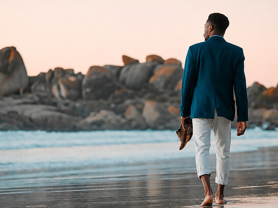 A businessman walks barefoot along the beach at sunset, carrying his shoes as he embraces a moment of peace, freedom, and reflection by the ocean