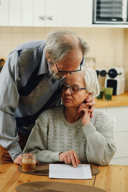 An elderly couple reads a document in the kitchen while sharing a moment of laughter, reflecting the warmth of a long-term relationship