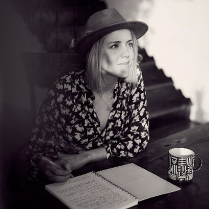 In this captivating monochrome image, a distinguished woman author, wearing a fashionable hat, finds solace in her writing, seated comfortably on a chair, her pen dancing across the paper, a reflection of her literary prowess and artistic spirit