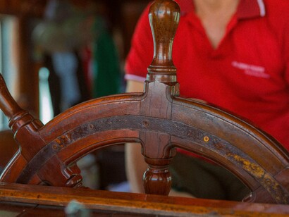 Roda do leme. Quando a embarcação parou, todos os turistas começaram a se levantar, se despedindo uns dos outros, bebendo mais uma taca de vinho com pressa, mas eu permaneci sentada, com as pernas no ar para evitar algum torpeço embriagado