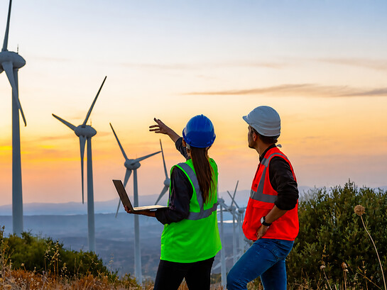 A team of young maintenance engineers works at a wind turbine farm at sunset, inspecting and maintaining the equipment