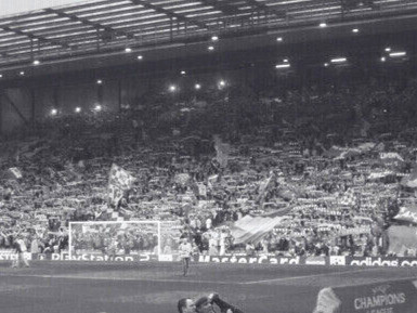 Une nuit européenne magique à Anfield. Les supporters des Reds dans le célèbre Kop lors d'une rencontre de Ligue des Champions, entourés de drapeaux et d'écharpes celebrant le Liverpool FC