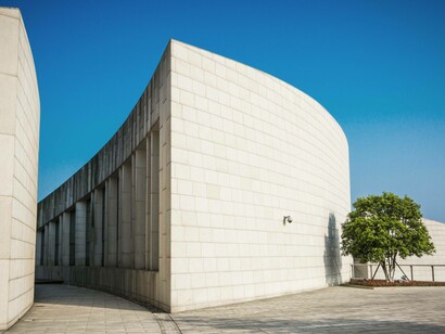 Un moderno edificio curvilineo, rivestito in pietra chiara, con pavimentazione esterna in lastre di cemento