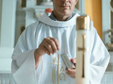 Inside the church, a priest prays as he lights a candle