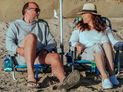 Mulher relaxa com amigos na praia. A boa notícia é que os sonhos não têm prazo de validade. Eles esperam por você. E a maturidade traz um presente único: a coragem de ouvi-los