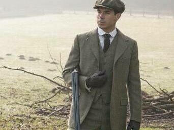 A man in the English countryside is wearing tweed and holding a hunter's rifle