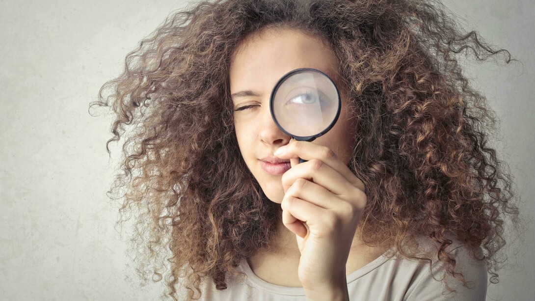A portrait of a woman holding a magnifying glass over her eye