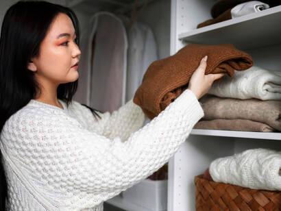 A woman is carefully organizing her closet, sorting through her clothes and arranging them by style and color to create a more streamlined and accessible space