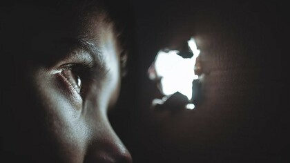 A person peering through a hole with a look of fear and uncertainty