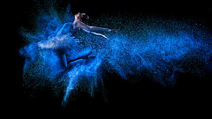 A young dancer leaps gracefully through a cloud of vibrant blue powder, creating a striking display of movement and artistic expression