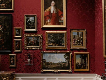 A museum gallery with historical artwork on deep red walls, featuring soft lighting, illustrating effective art gallery illumination and exhibition space lighting