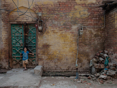 A child leans against a doorway in an urban neighborhood in Pakistan, reflecting everyday life amid poverty