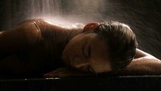 A woman relaxing in a spa beneath a cascading waterfall, resting on a marble surface with her eyes closed in tranquility