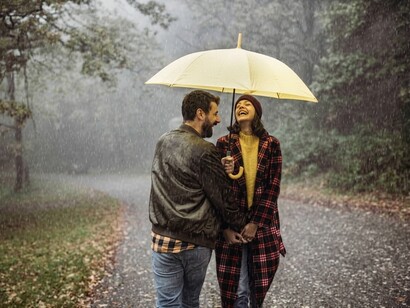 A loving couple embraces beneath an umbrella while walking through a misty autumn forest