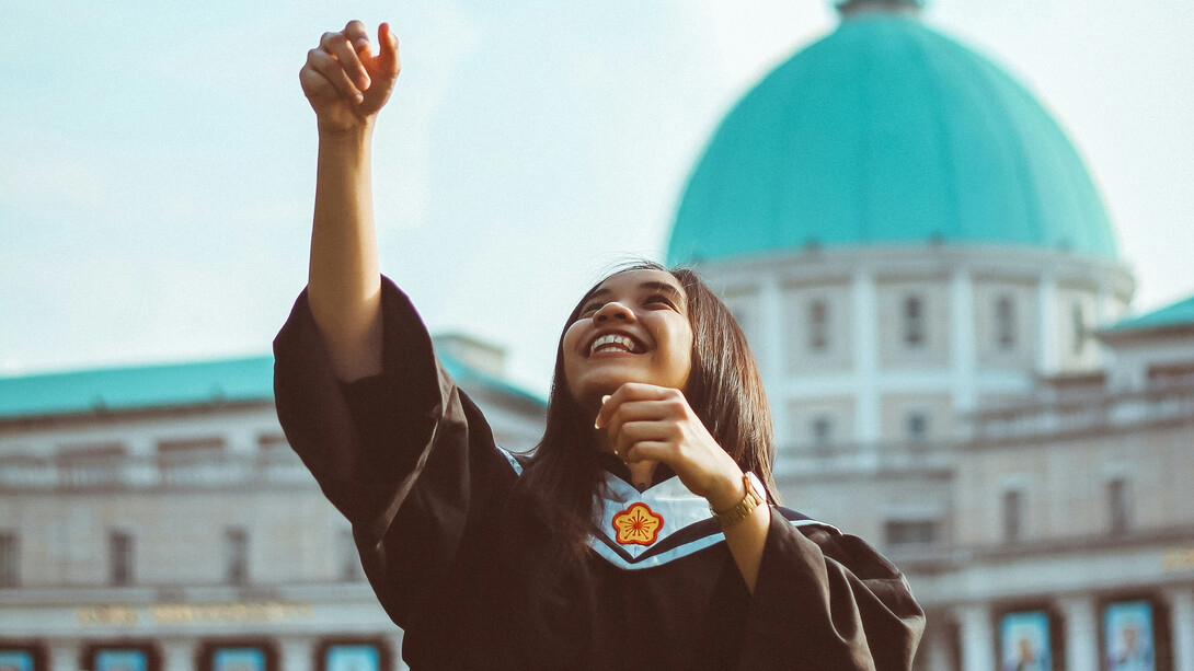 A young girl celebrates in her academic dress, a wide smile on her face