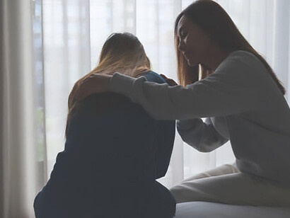 A comforting sister embraces, holds, and encourages a woman in the bedroom after a nightmare