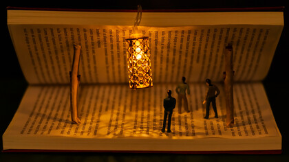 Miniature people and a lamp inside a half-open book