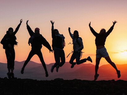 Silhouetted figures raise their hands in joy as the sun sets during golden hour