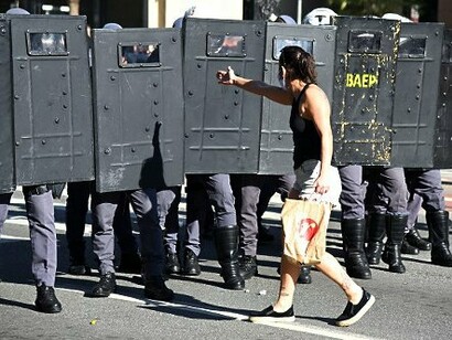 Frente a frente com o cordão policial, a manifestante simboliza o encontro entre a expressão do dissenso e os mecanismos institucionais de manutenção da ordem. O artigo propõe refletir sobre as disputas políticas e epistemológicas que moldam o mundo contemporâneo