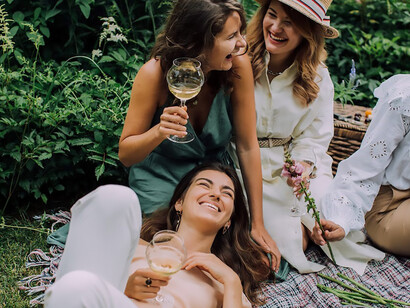 Four women lounging on the grass, toasting with glasses of wine, joyously celebrating Galentine's Day and reveling in the warmth of their friendship