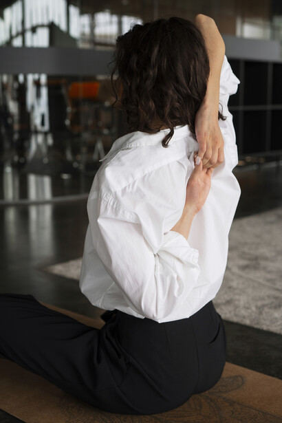 A woman stretching at her desk, showing signs of fatigue and poor posture from long hours of desk work