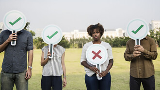 A dissatisfied Black woman gazes directly at the camera, holding a sign shaped like a cross