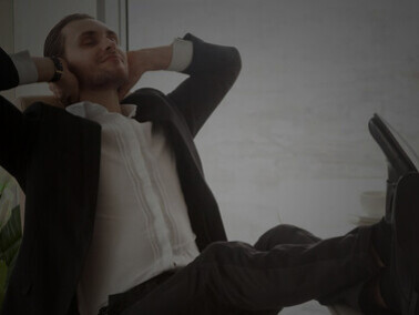 A smiling businessman relaxes in a contemporary office, using mindfulness practices, stress relief techniques, and breathing exercises to manage anxiety and improve his mental well-being