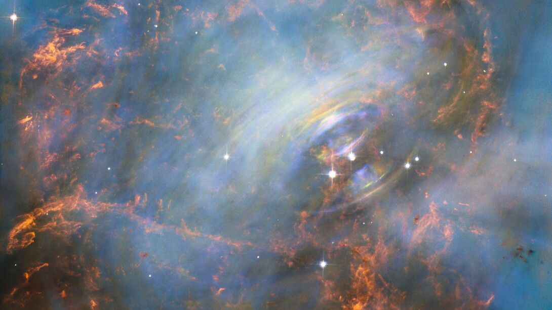 Mentre molte altre immagini della famosa Nebulosa del Granchio si sono concentrate sui filamenti nella parte esterna della nebulosa, questa immagine mostra il cuore stesso della Nebulosa del Granchio, compresa la stella di neutroni centrale — che è la più a destra delle due stelle luminose vicine al centro di questa immagine. Il rapido movimento del materiale più vicino alla stella centrale è rivelato dal delicato arcobaleno di colori presente in questa immagine realizzata con la tecnica del time-lapse; l’effetto arcobaleno è dovuto al movimento del materiale nel lasso di tempo che intercorre tra una foto e l’altra. Fonte NASA, ESA