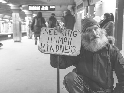 A sign revealing hope for progress in humanity as a man holds up "seeking human kindness" as a note to the world