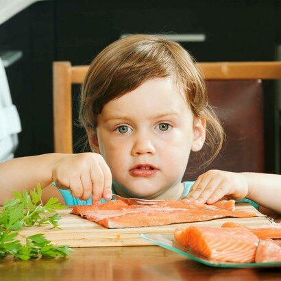 Bambino con un tagliere di salmone: "Gli acidi grassi Omega-3, presenti per esempio nel pesce, nei semi di lino e nelle noci riducono l’infiammazione intestinale"