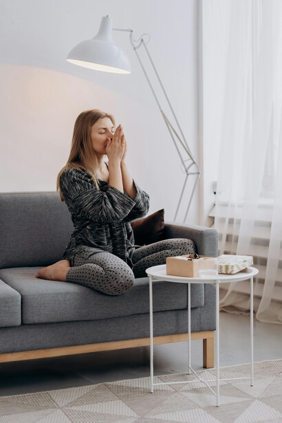 A woman wearing a black-and-white long-sleeve dress sits on a grey couch at home