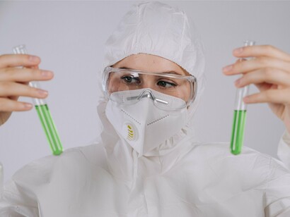 Pesquisadora, protegida por óculos e equipamentos de segurança, observa atentamente uma amostra em um tubo de ensaio. A análise laboratorial é fundamental para identificar substâncias presentes em concentrações muito pequenas