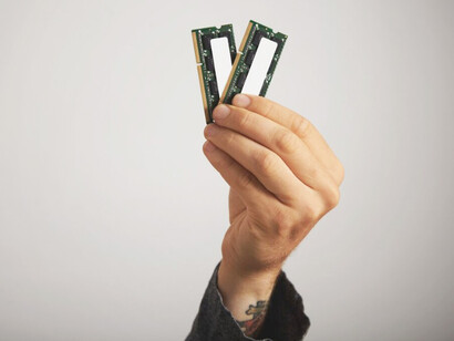 Close-up of a man in a dark grey long-sleeve shirt holding a blank memory chip against a white background