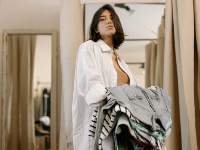 Mulher escolhe roupas em uma loja, carregando diversos cabides nas mãos. O consumo consciente começa com escolhas feitas antes de chegar ao caixa