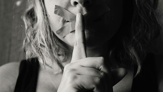 A woman places her finger on her already duck-taped lips