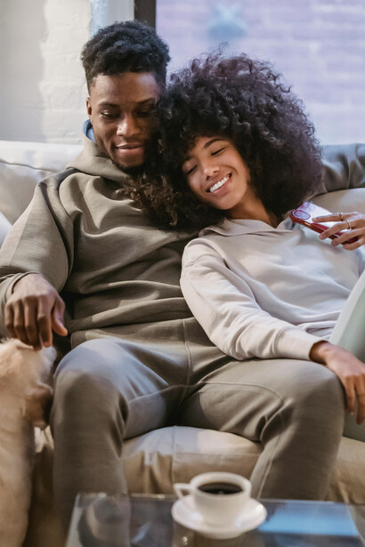 Happy Black couple sitting on a couch, watching a vertical microdrama on a smartphone