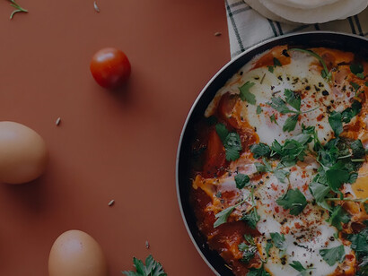 On the table, a sizzling pan cradles a picturesque display of shakshuka, its rich and inviting colors creating an appetizing scene