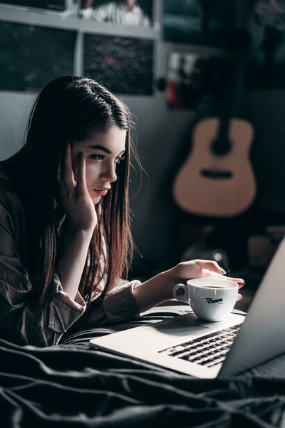 A girl sitting on her bed, drinking coffee and staring at her laptop's screen. In Russia there are now widespread restrictions across multiple social media platforms and internet services