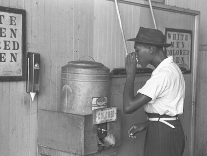 A colored man drinking at "Colored" water cooler in streetcar terminal, Oklahoma City, USA