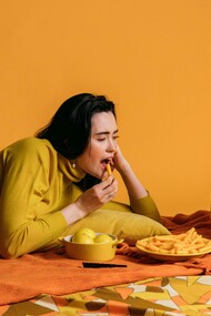 A woman in a yellow long-sleeve shirt watches TV while eating, binge-watching