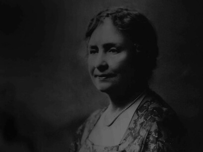 A younger Helen Keller posing for a portrait wearing a pearl necklace 