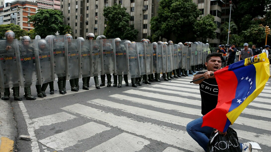 Joven con una bandera venezolana ante un grupo de policías antidisturbios