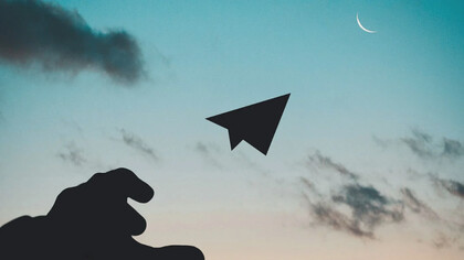 Un ragazzo lancia un aeroplano di carta in direzione del cielo, verso la luna 