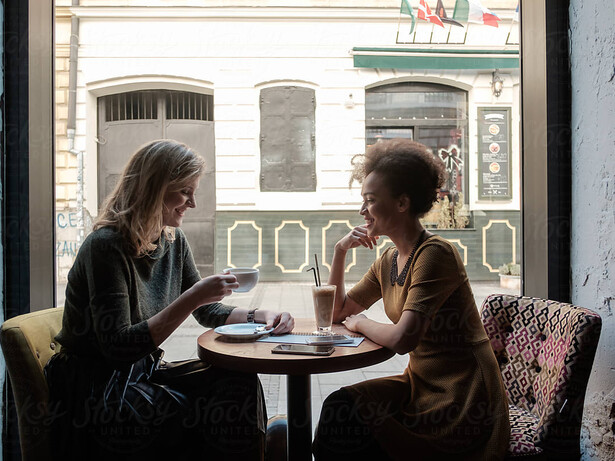 Two women share an emotional reunion in a café, laughing together