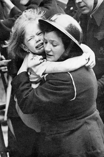 A female warden carrying a little girl after she had been rescued by a fireman from a house on which a V1 flying bomb had landed in Southern England