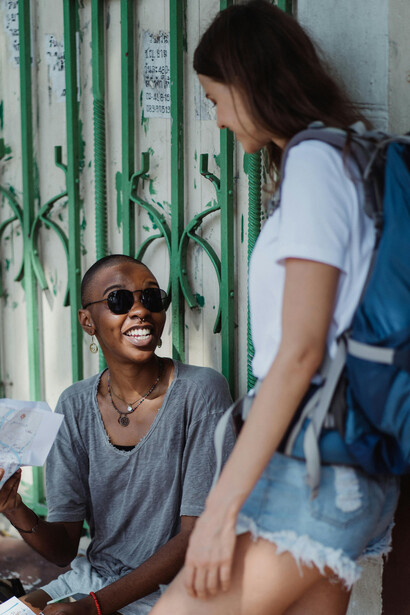 Two women exploring a vibrant urban area, wearing backpacks and looking at a map as they navigate the city together